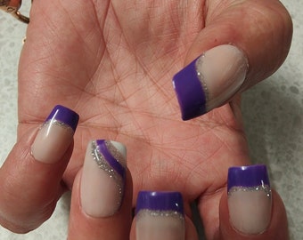Op de afbeelding: Close-up van een hand met vijf vingernagels die zijn geverfd met een lichtroze basis en een paarse en zilveren glittertop. De nagels zijn vierkant met afgeronde hoeken.