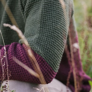May include: A close-up of a green and purple waffle knit sweater. The sweater is made of a soft, comfortable material and has a relaxed fit.
