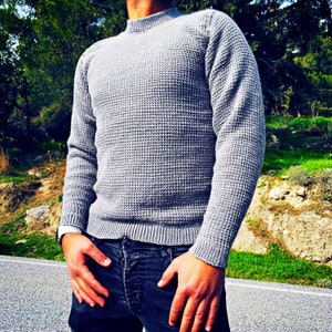 May include: A gray waffle knit sweater with a mock neck and long sleeves.