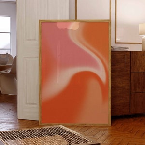 May include: A framed abstract art print with a peach and pink gradient background. The print is in a wooden frame and is hanging on a wall in a living room.