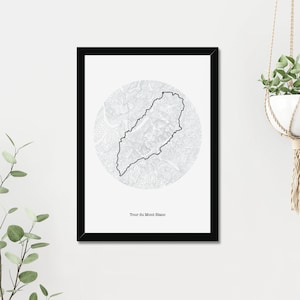 May include: Black and white print of a topographic map of the Tour du Mont Blanc, a famous hiking trail in the Alps. The print is framed in a black frame and has the text "Tour du Mont Blanc" at the bottom.
