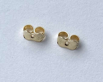 May include: Two gold-toned earring backs. The backs are made of metal and have a small hole in the centre.