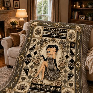 Könnte beinhalten: Eine gesteppte Tagesdecke mit einer zentralen Illustration von Betty Boop in einem gepunkteten Kleid und schwarzen Handschuhen. Das Design zeigt komplizierte Muster aus Rosen, Schleifen, Herzen und perlenartigen Schnüren in Grau, Schwarz und Creme.