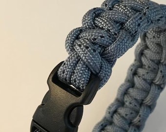 May include: A gray paracord bracelet with a black plastic buckle.