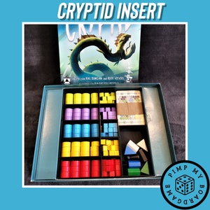 Könnte beinhalten: Ein blauer und grüner Spieleinsatz für das Spiel "Cryptid" mit Fächern zum Verstauen der Spielsteine. Der Einsatz ist aus Schaumstoff und hat ein individuelles Design, das in die Spielbox passt. Der Einsatz wurde entwickelt, um die Spielsteine zu organisieren und zu verstauen, was das Einrichten und Spielen des Spiels erleichtert.