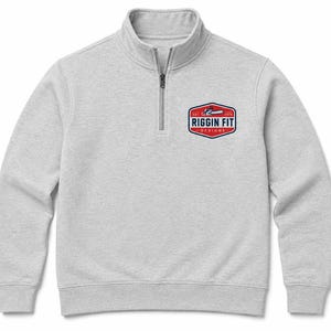 May include: A light gray quarter-zip sweatshirt featuring a red, white, and blue logo on the left chest. The logo is a shield shape containing a chainsaw graphic, the text RIGGIN FIT, the word DESIGNS, and the text EST. 2006 in dark blue lettering.