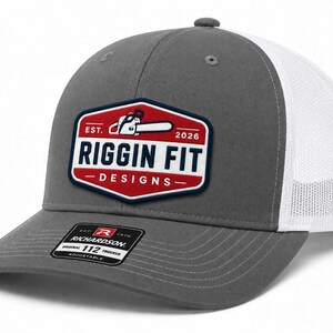 May include: A grey and white trucker hat featuring a red, white, and blue patch on the front. The patch displays a chainsaw icon, the text EST. 2026, and the words RIGGIN FIT DESIGNS. A black sticker on the brim reads RICHARDSON 112 TRUCKER.