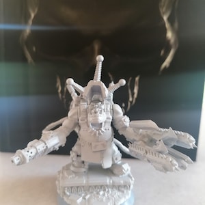 May include: A white plastic model of an Ork, a fictional race of green-skinned humanoids from the Warhammer 40,000 universe. The Ork is holding a large gun in one hand and a pair of blades in the other. The model is unpainted and ready to be assembled.