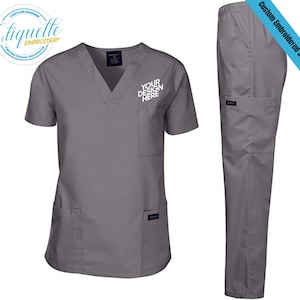 May include: Gray scrub top and pants set with a v-neck and short sleeves. The top has a pocket on the left chest and two pockets on the bottom. The pants have two side pockets and one back pocket. The text "YOUR DESIGN HERE" is embroidered on the top.