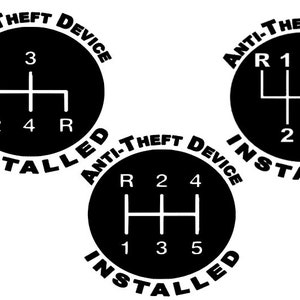 Może przedstawiać: Trzy okrągłe naklejki w kolorze czarnym i białym z tekstem "ANTI-THEFT DEVICE INSTALLED" wokół krawędzi. Każda naklejka zawiera stylizowane zdjęcie schematu zmiany biegów w samochodzie.