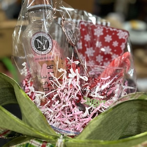 May include: A clear glass bottle with a rose gold lid and a label that says "Cocktail Infusion Mixer, New York, Just Add Rose Wine". The bottle is in a clear plastic bag with pink and white shredded paper, a red and white patterned fabric, and a red candy cane.
