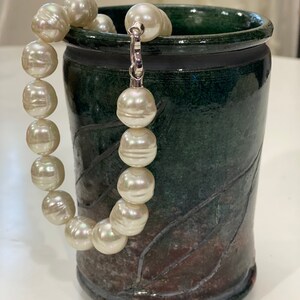 May include: A white pearl necklace with a silver clasp, resting in a green ceramic mug with a brown glaze.