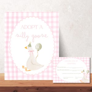May include: A pink and white gingham background with a large card that says "ADOPT A silly goose". The card features a watercolor illustration of a goose wearing a party hat and holding a balloon. A smaller certificate of adoption is also included.