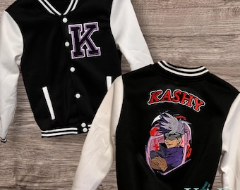 Puede incluir: Una chaqueta universitaria negra y blanca con una letra K morada en el pecho. La parte posterior muestra el nombre KASHY en letras rojas sobre una ilustración gráfica de un personaje de anime con pelo gris y una venda negra.