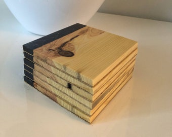 May include: A set of six wooden coasters with a black edge. The coasters are stacked on top of each other and have a natural wood grain.