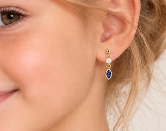 May include: A gold drop earring featuring a small white spherical bead at the top and a marquise-shaped blue gemstone suspended below. The earring is attached to a gold post that secures the piece to the earlobe with a simple, elegant design.