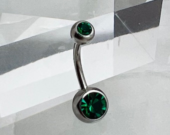May include: A silver belly button ring with two green gem stones.