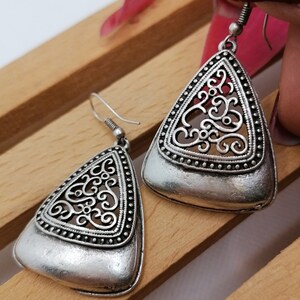 May include: A pair of silver triangle-shaped earrings with a delicate filigree design. The earrings have a smooth, polished finish and are accented with small beads around the edges.