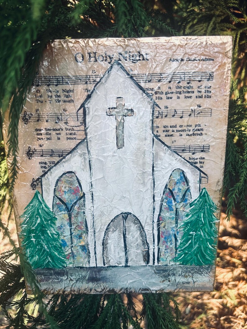 Puede incluir: Pintura hecha a mano de una iglesia blanca con una cruz, sobre un fondo de partituras antiguas. La obra presenta vidrieras y dos &aacute;rboles de Navidad verdes. El texto "O Holy Night" es visible.