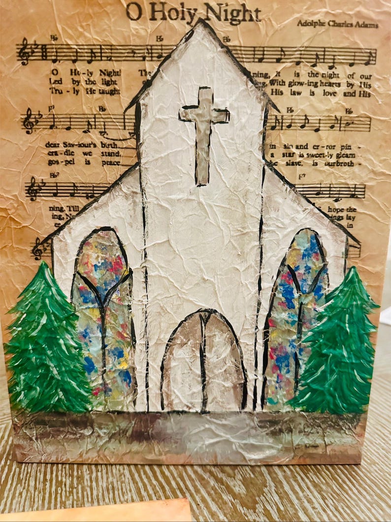 Puede incluir: Una obra de arte navide&ntilde;a hecha a mano que representa una iglesia blanca con una cruz, vidrieras y &aacute;rboles de Navidad verdes. El fondo es una partitura musical con el texto "O Holy Night". La obra est&aacute; sobre una superficie texturizada.