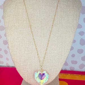 Puede incluir: Un collar de cadena dorada con un gran colgante en forma de corazón iridiscente.