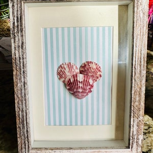 May include: A framed seashell art piece with three pink and white seashells arranged in a heart shape on a blue and white striped background.