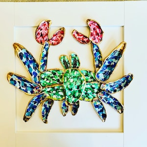 Puede incluir: Una colorida obra de arte de un cangrejo con un marco blanco. El cuerpo del cangrejo está pintado de verde, las pinzas son rojas y las patas azules. El borde dorado perfila la forma del cangrejo, creando un vibrante tema costero.