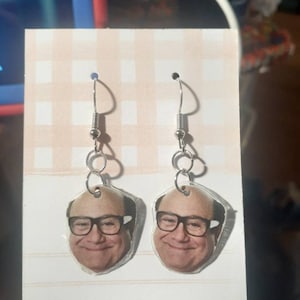 May include: A pair of silver dangle earrings with a photo of a man with glasses on each earring.