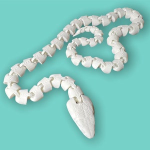 May include: White plastic articulated snake toy. The snake is made up of many connected segments and has a pointed head.