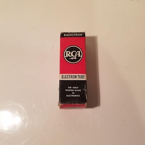 May include: A vintage Radiotron RCA Electron Tube box. The box is red with a black top and bottom. The RCA logo is in a white circle on a red background. The text "ELECTRON TUBE" and "THE MOST TRUSTED NAME IN ELECTRONICS" are also visible.