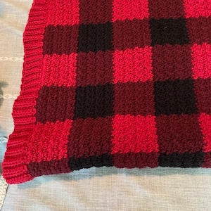Puede incluir: Una manta de crochet de cuadros rojos y negros con un borde de flecos.