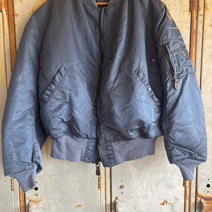 Puede incluir: Una chaqueta bomber azul oscuro con cierre de cremallera y un parche en la manga izquierda que dice "U.S. AIR FORCE".