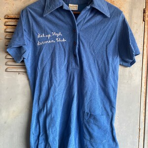 以下が含まれることがあります： 白い刺繍で「Sal. Up. High. Thurman Club.」と書かれたロゴが付いた、青い半袖ポロシャツです