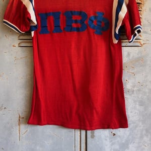 Camisa gráfica vintage Pi Beta Phi (M) Camiseta vintage Ringer vermelha com decote azul e branco, manga com logotipo, bainha da camisa universitária, ponto único, letra K