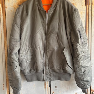 May include: A green bomber jacket with a zipper closure and an orange lining. The jacket has a ribbed collar, cuffs, and waistband.