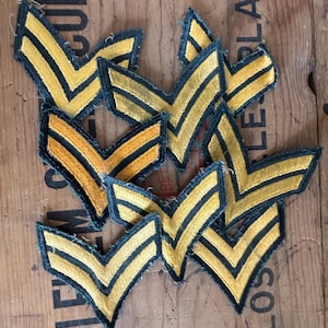 May include: A collection of yellow and black chevron patches. Each patch features a yellow chevron design with black stripes and a dark green border. The patches are scattered on a wooden surface.
