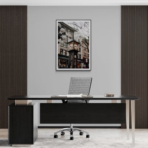 K&ouml;nnte beinhalten: Ein schwarzer Schreibtisch mit einem wei&szlig;en B&uuml;rostuhl davor. An der Wand hinter dem Schreibtisch h&auml;ngt ein gerahmtes Foto eines Uhrturms in einer Stadt.