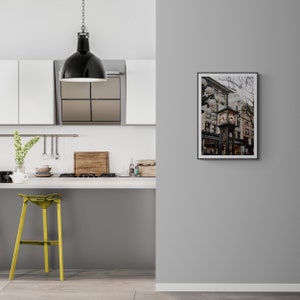 K&ouml;nnte beinhalten: Eine schwarze Pendelleuchte h&auml;ngt &uuml;ber einer K&uuml;chentheke mit einem gelben Hocker. An der Wand h&auml;ngt ein gerahmtes Foto eines Uhrturms in einer Stadt.