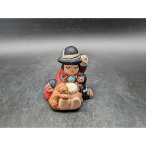 May include: A white ceramic mug with a black handle and the text "But First, Coffee" in a bold, black font. The mug is set against a blurred background, suggesting a cozy setting.