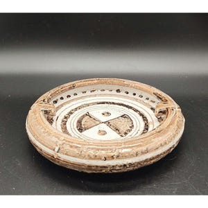 May include: A white ceramic ashtray with a brown geometric design. The ashtray has a raised rim and a circular shape.