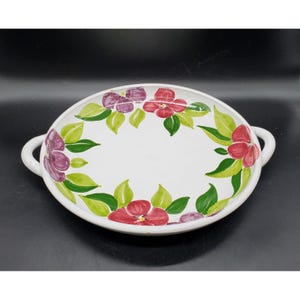 May include: White ceramic serving dish with two handles. The dish is decorated with a floral pattern of red, purple, and green flowers.