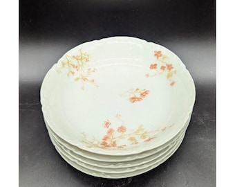 May include: A stack of five white ceramic bowls with a scalloped edge. Each bowl is decorated with a delicate floral pattern in shades of peach and green. The bowls are stacked on a dark surface.