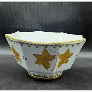 May include: White porcelain bowl with a geometric shape and gold leaf design. The bowl features a scalloped rim and a pedestal base. Gold leaf accents adorn the exterior, including the rim and the base. The bowl's design includes gold-coloured leaves.