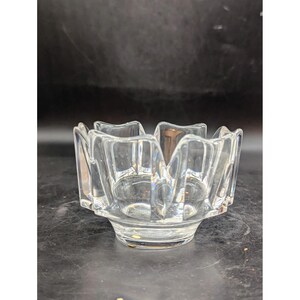 May include: A clear glass bowl with a unique, geometric design. The bowl has a scalloped edge and a wide, flat base.