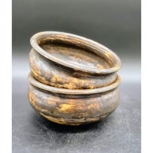 May include: Two stacked, antique-style bowls with a dark brown and gold metallic finish. The bowls have a rounded shape with a slightly flared rim. The metallic finish gives the bowls a rustic, aged appearance.