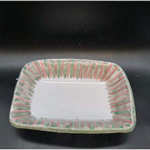 May include: Rectangular ceramic dish with a white interior and a green and red striped border. The dish has rounded corners and is likely used for serving food or displaying small items.
