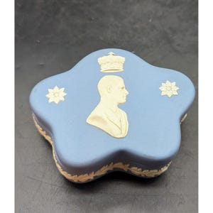 May include: A blue and white ceramic trinket box with a raised design of a man's bust, a crown, and two flowers. The box is shaped like a star.