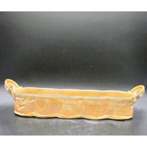 May include: A rectangular, handmade ceramic tray with a light brown glaze. The tray features two curved handles and a wavy edge design. The interior is a slightly darker shade of brown. This decorative tray is ideal for serving or display.