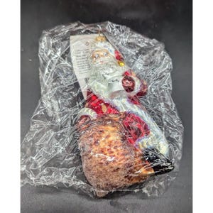 Peut inclure: Ornement de Noël représentant le Père Noël, emballé dans du plastique transparent. Il porte un costume rouge avec des bordures blanches et une barbe blanche. L'ornement a une base marron et des bottes noires. Une boucle dorée est en haut pour l'accrocher.