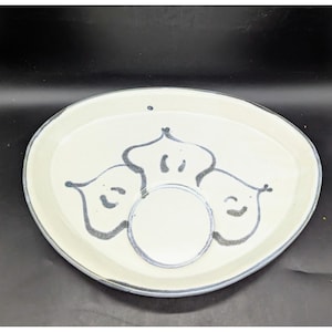 May include: Oval ceramic serving platter with a cream-colored surface and a blue rim. The platter features a central circular indentation and three stylized, dark blue floral or leaf-like designs.